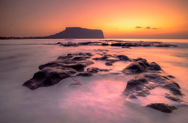 Amanecer sobre el pico Seongsan Ilchulbong, en la isla de Jeju, con rocas volcánicas en el mar